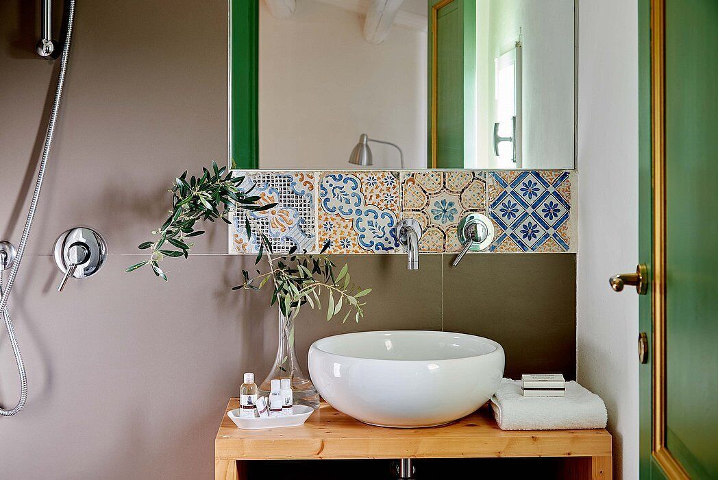 Een badkamer met een grote witte wastafel, een spiegel, een douche en een betegelde spatwand.