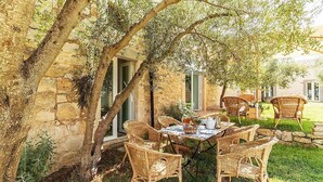 An outdoor dining area with wicker chairs and a table set for four, surrounded by stone walls and greenery.