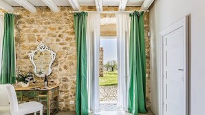 A room with a stone wall, a wooden desk, a white chair, and a view through a glass door.