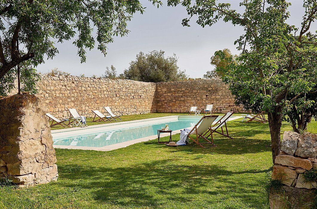 Piscina com espreguiçadeiras e um muro de pedra.