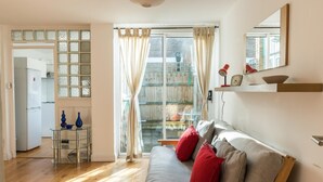 A cozy living room with a sofa, a glass coffee table, and a view through a large window. - Super 1BD Garden Flat Islington London (London)