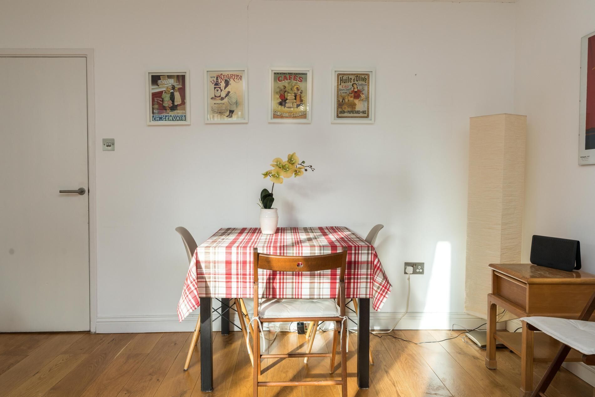 A dining area with a table set for two, a vase with flowers, and a wall with vintage posters.