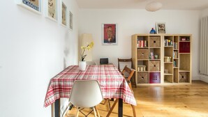 A dining area with a red and white checkered tablecloth, a white chair, a bookshelf with various items, and a poster on the wall. - Super 1BD Garden Flat Islington London (London)