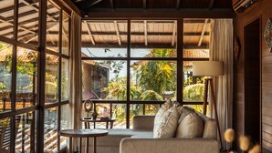 A room with a wooden ceiling, a ceiling fan, a sofa, a table, and large windows. - Grün Ubud (Ubud)