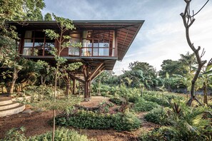 Una casa de madera con balcón, rodeada por un jardín con diversas plantas y árboles.