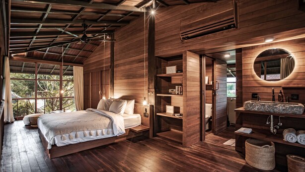 A spacious bedroom with a large bed, wooden walls, and a built-in vanity with a mirror. - Grün Ubud (Ubud)