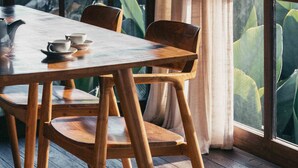 A wooden dining table with chairs, a hanging light fixture, and a view of lush greenery through large windows. - Grün Ubud (Ubud)