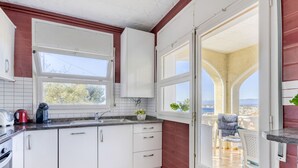Cocina con armarios blancos, ventana y vista a un balcón con una silla.