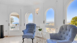 Amplia habitación con dos sillones grandes, una mesita y vistas a un paisaje urbano a través de ventanales arqueados.
