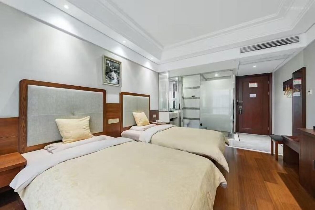 A hotel room with two beds, a wooden headboard, a mirror, and a door leading to a bathroom.