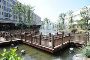 Une cour avec une fontaine, un pont en bois et des bâtiments qui l’entourent.