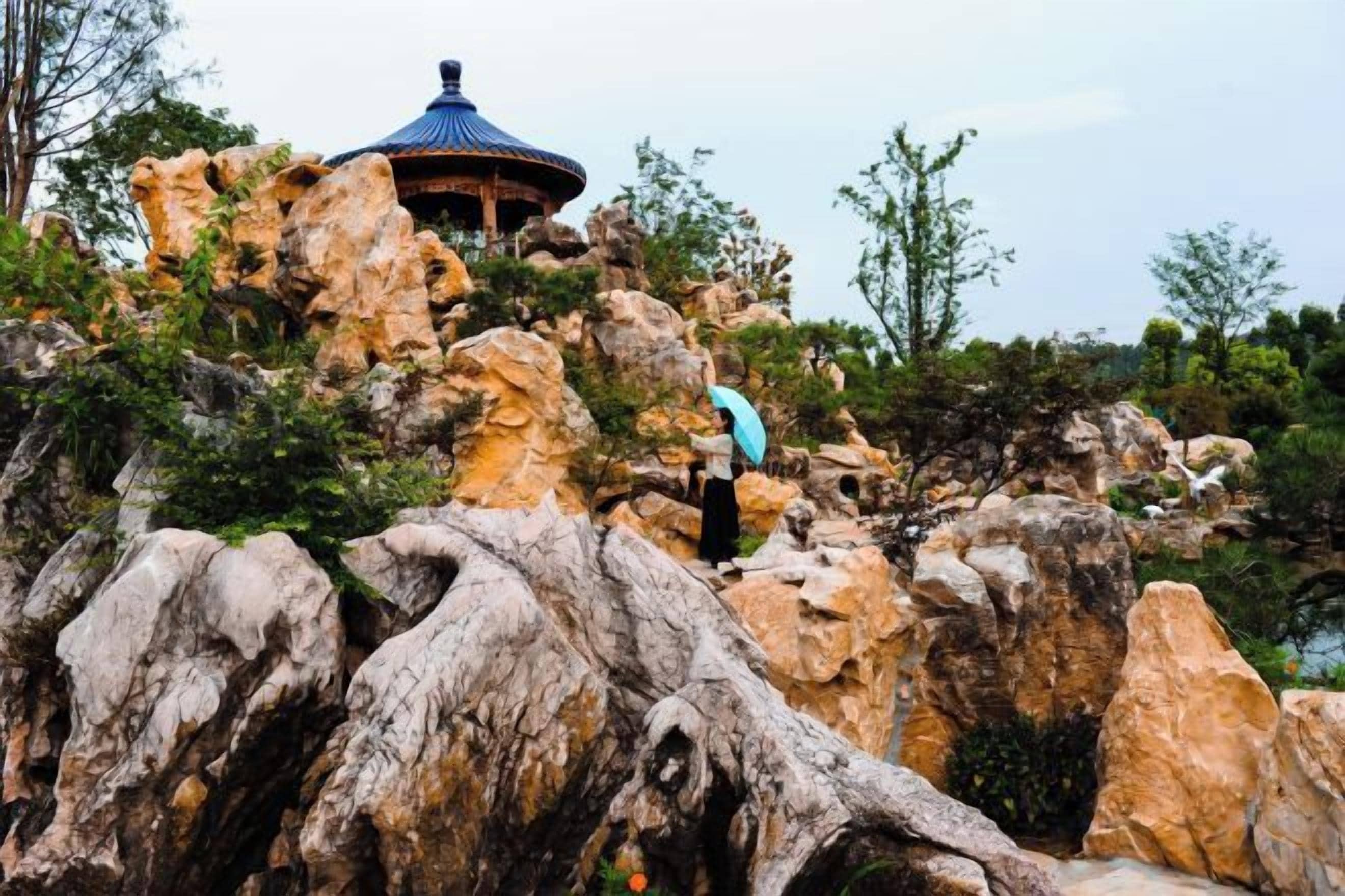 A rock formation with a gazebo on top, surrounded by trees.