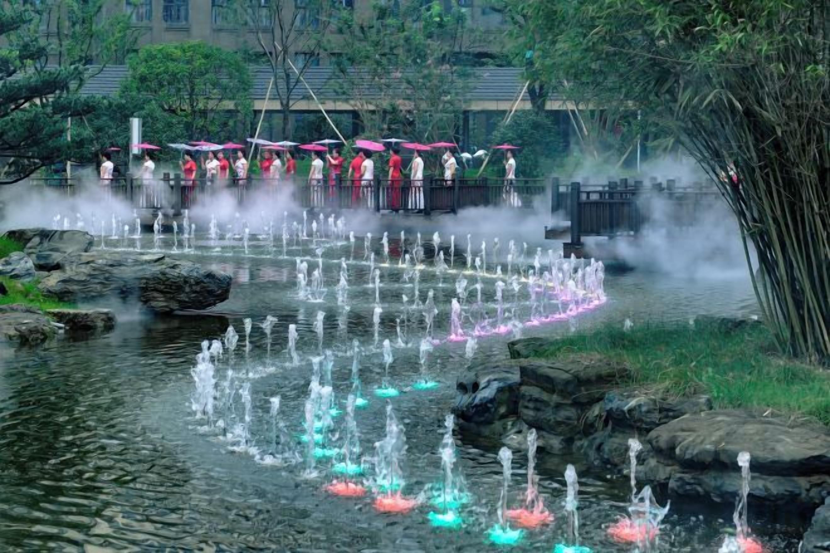 Un élément décoratif aquatique composé de fontaines et d’un pont où se trouvent des personnes portant des costumes traditionnels.