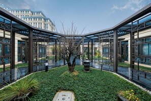 A courtyard with a central tree, glass walls, and a metal roof structure. - Heye Hotel (Anji)