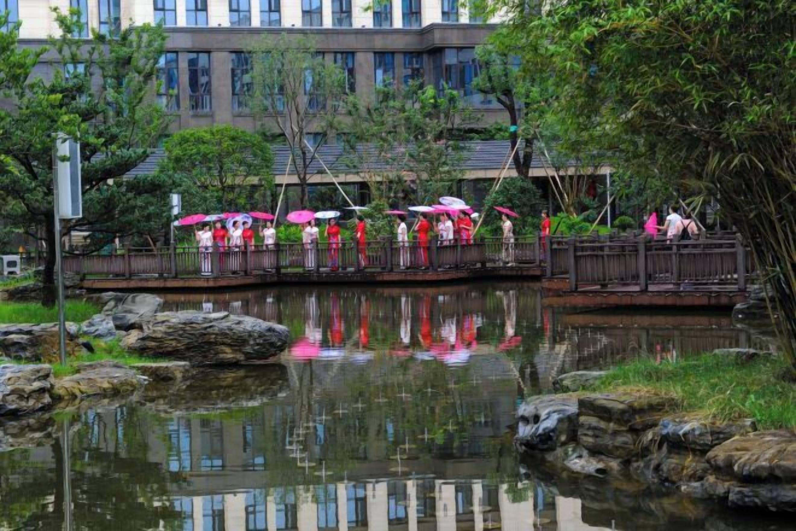 A bridge over a calm body of water with people walking, a building in the background, and a reflection on the water.