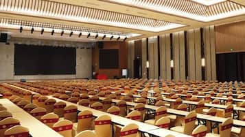 Une salle de conférence avec des rangées de tables et de chaises, une scène et un grand écran.