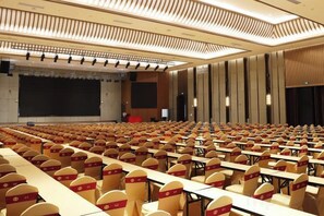 A conference room with rows of tables and chairs, a stage, and a large screen. - Heye Hotel (Anji)