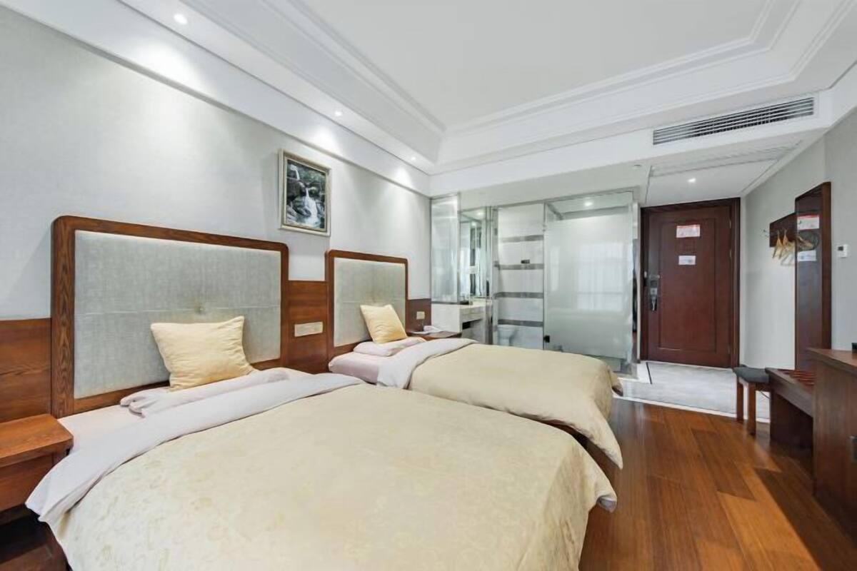 A hotel room with two beds, wooden headboards, a large mirror, a wooden desk, and a door.