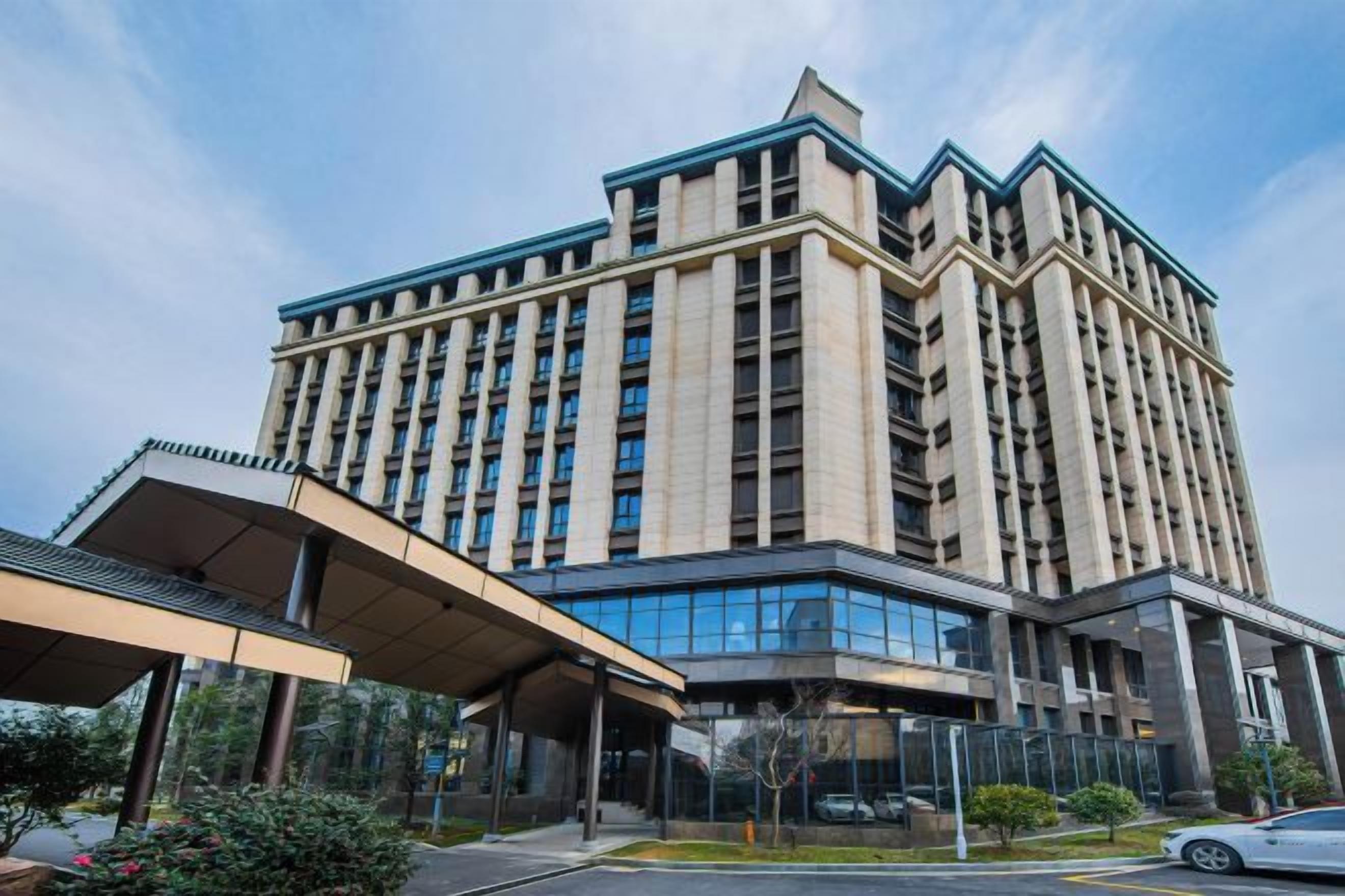 Un hotel de varios pisos con diseño moderno, que cuenta con una entrada cubierta y un área de estacionamiento.