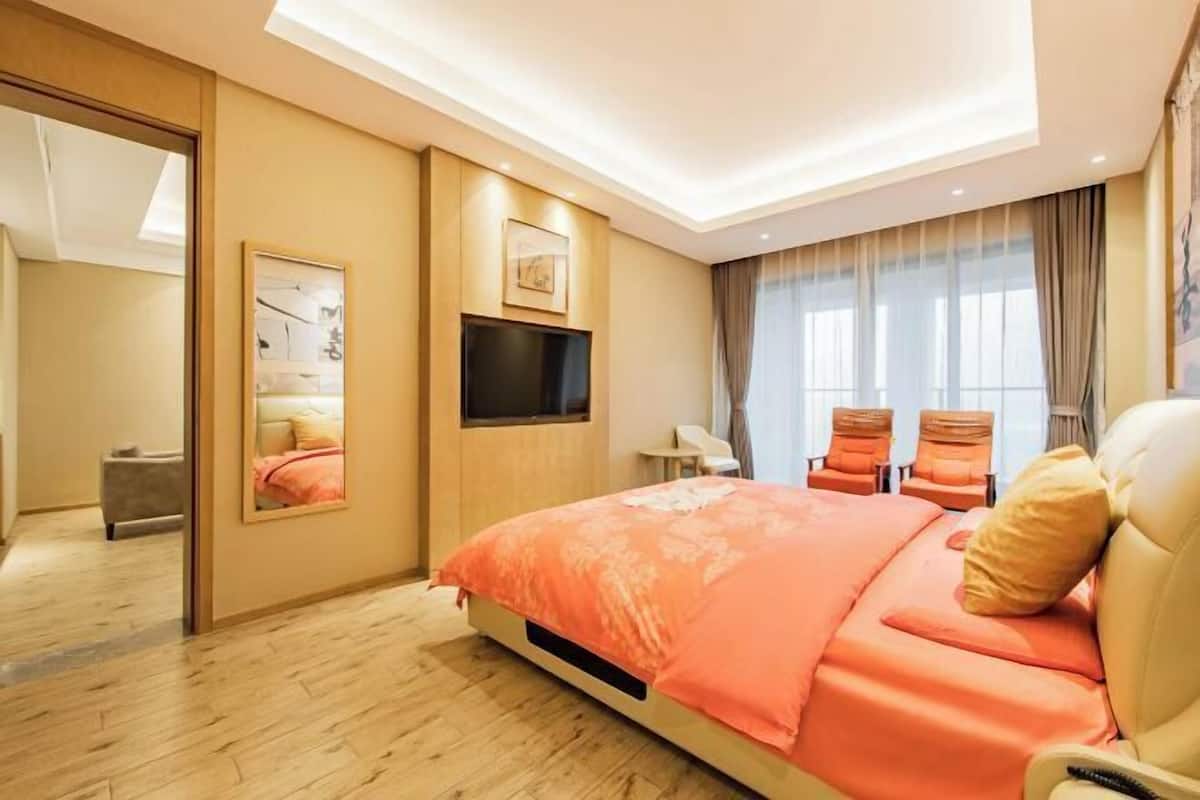 A modern hotel room with a large bed, a flat-screen TV, a seating area with chairs, and a large mirror.