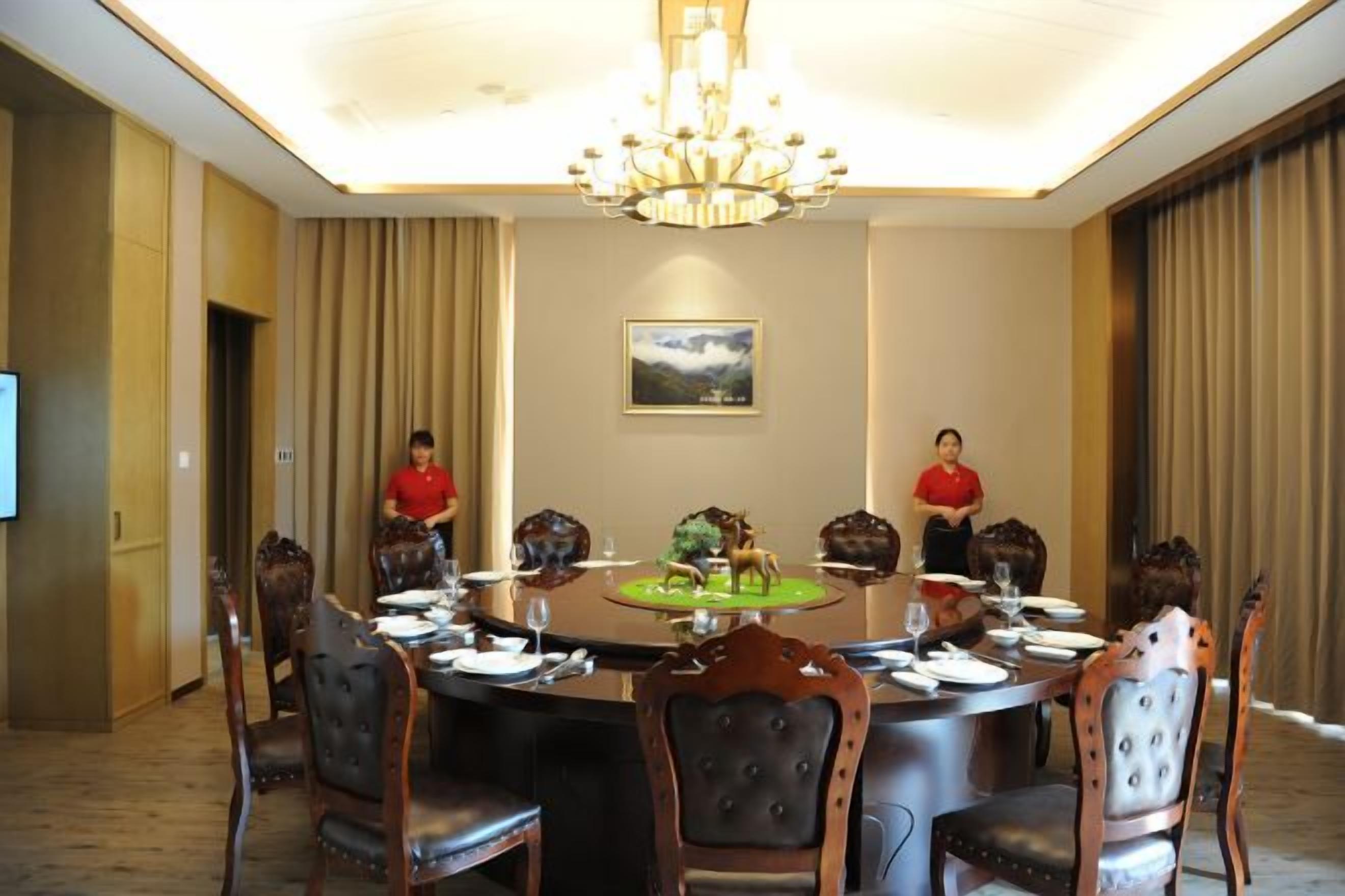 A conference room with a round table, chairs, a chandelier, and a television screen.