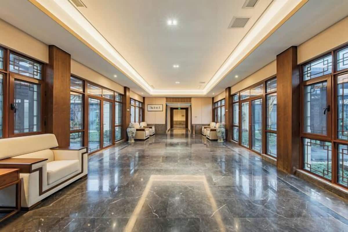 A spacious hallway with a polished marble floor, large windows, and a sofa with a side table.