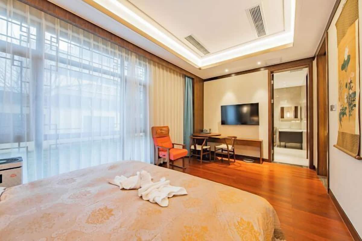A hotel room with a bed, a desk, a chair, a television, and a bathroom visible through an open door.