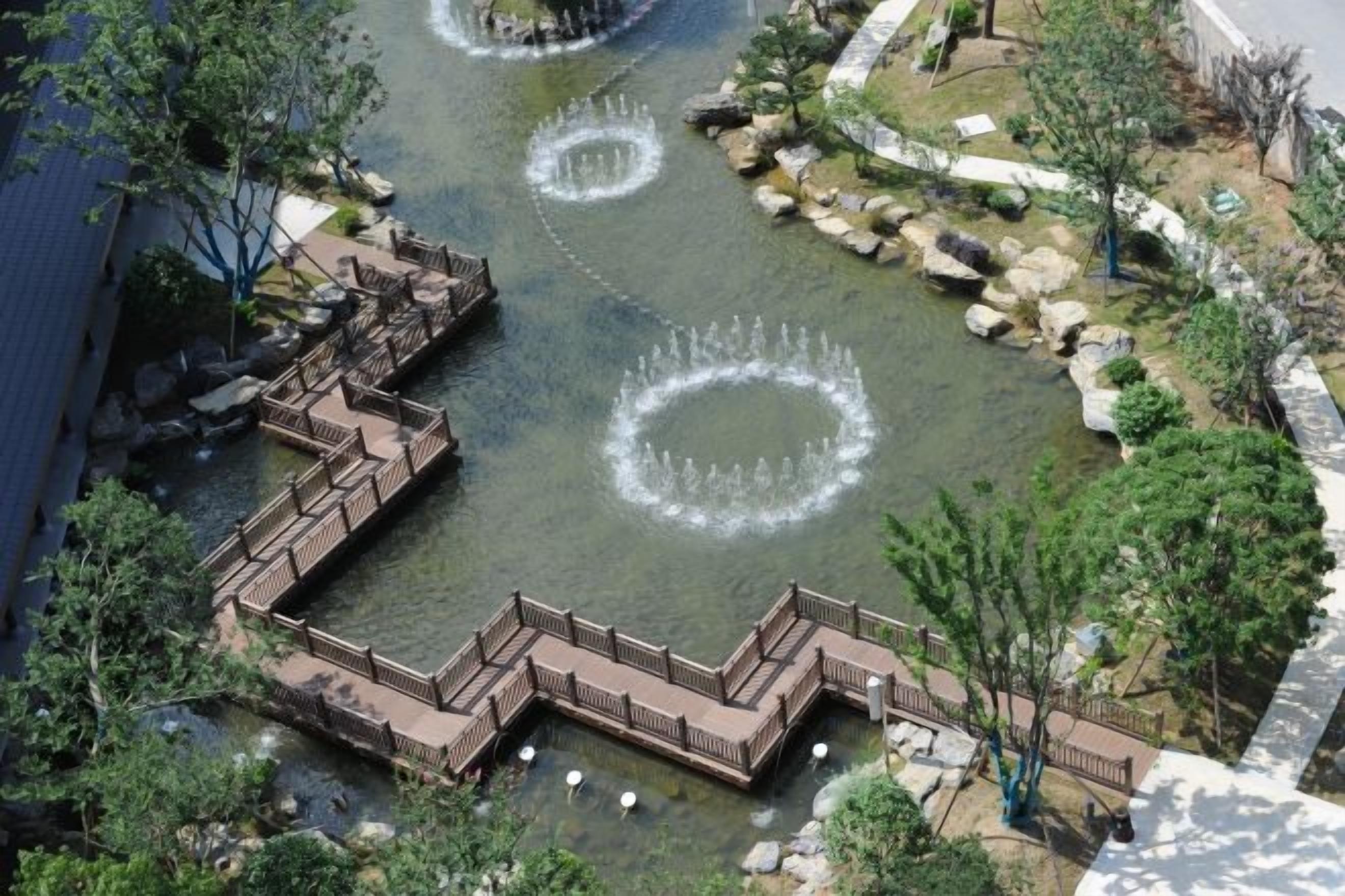 A water feature with circular fountains, a wooden deck, and surrounding greenery.