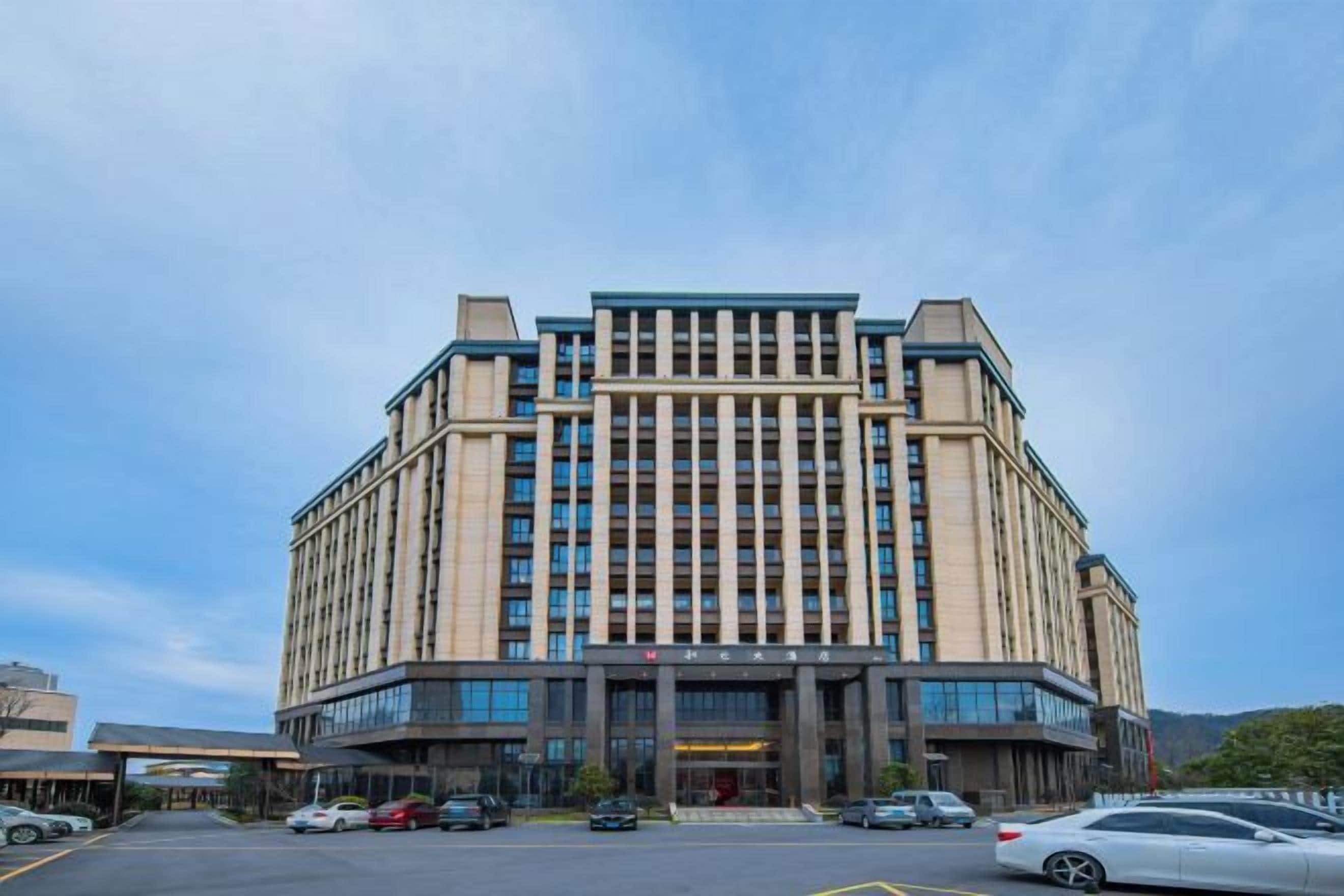 A multi-story hotel with a central entrance, large windows, and a parking lot.