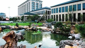 A modern building with a landscaped garden featuring a pond and rocks. - Heye Hotel (Anji)