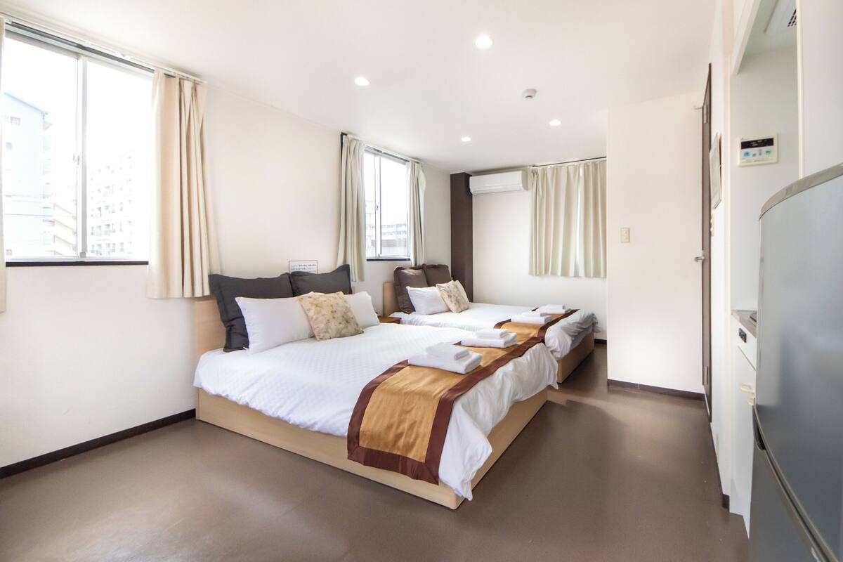 A hotel room with three beds, a large window, and a refrigerator.