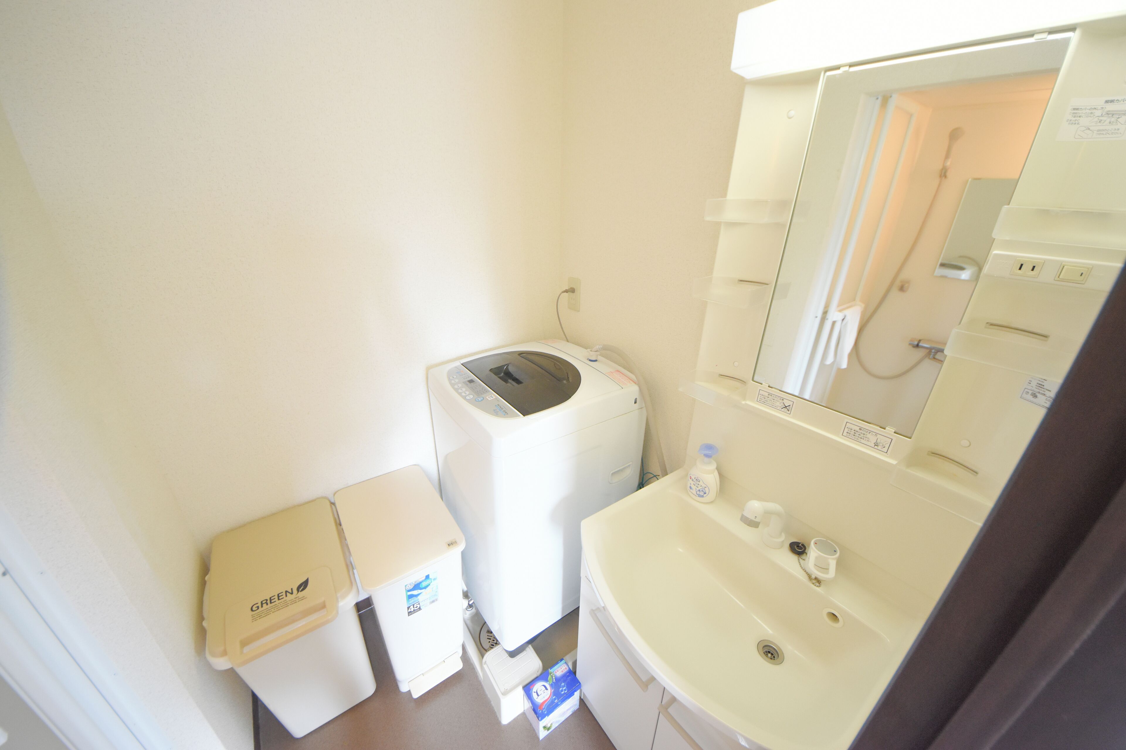 A compact bathroom with a washing machine, a small trash bin, and a sink with a mirror.