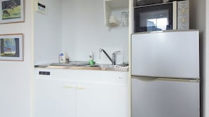 A compact kitchen with a built-in dishwasher, a microwave, and a sink. - Comfy Stay Kiyokawa (Nara)