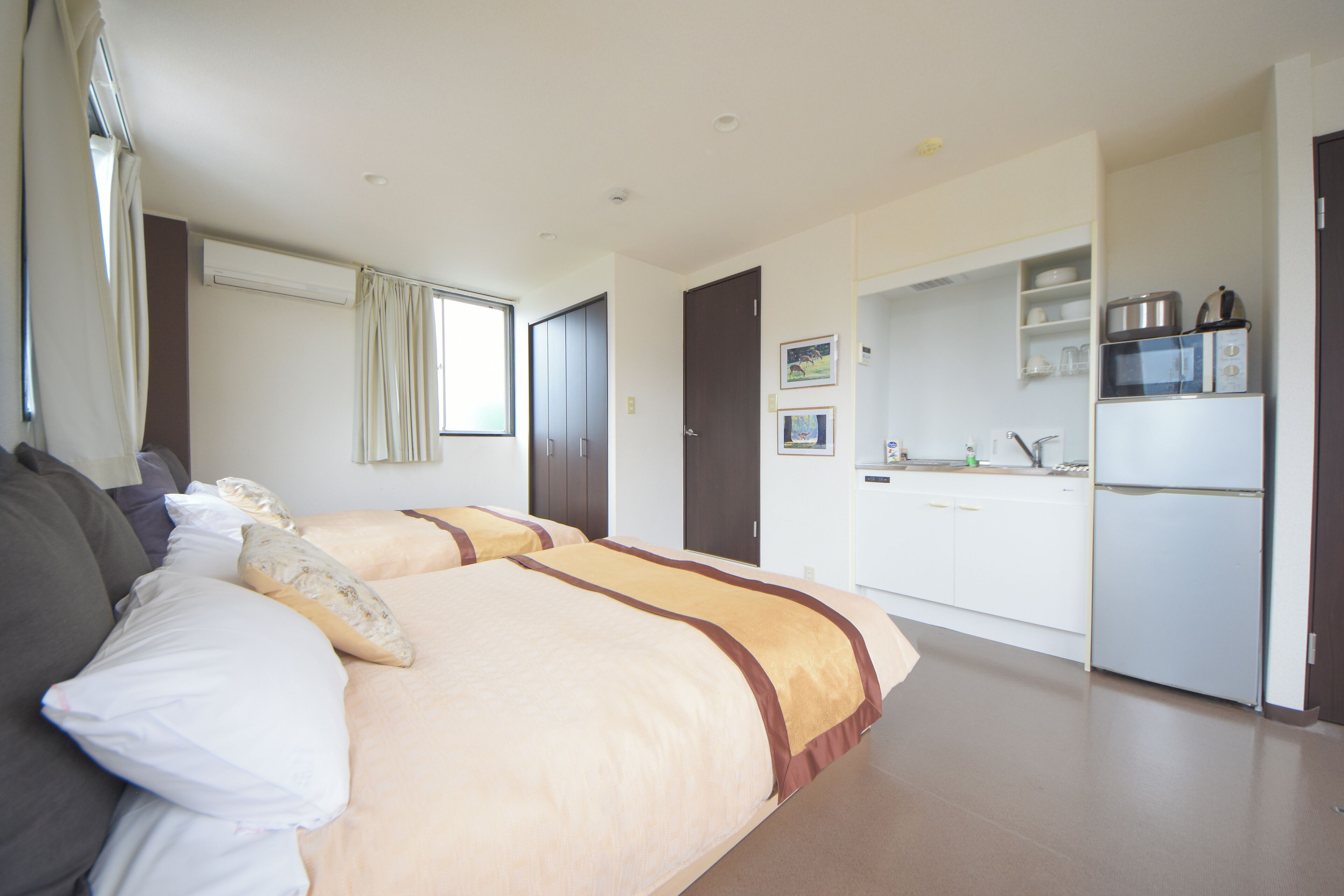A hotel room with two beds, a kitchenette, and a bathroom.