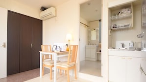 A compact kitchen with white cabinets, a dining table with chairs, and a small countertop. - Comfy Stay Kiyokawa (Nara)