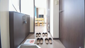A hotel hallway with a shoe rack, a television, and a dining area in the background. - Comfy Stay Kiyokawa (Nara)