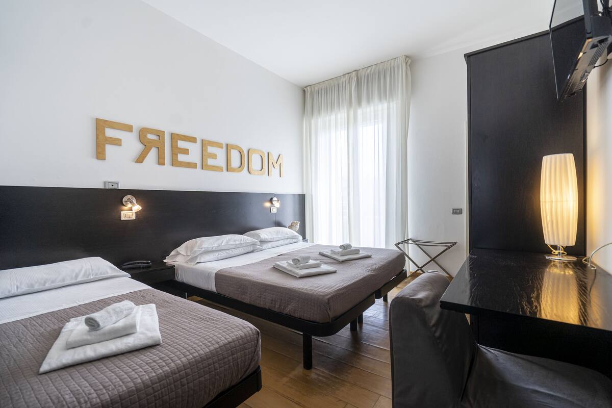 Ein Hotelzimmer mit zwei Betten, einem Schreibtisch und einem großen Spiegel.
