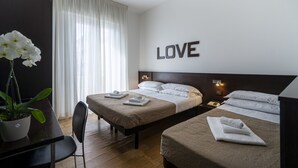 Habitación de hotel con dos camas, una planta en maceta, un escritorio y una pared con la palabra 'LOVE'.