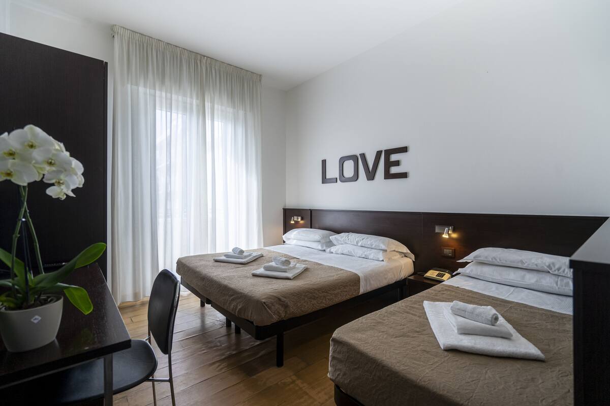 Ein Hotelzimmer mit zwei Betten, einer Topfpflanze, einem Schreibtisch und einer Wand mit dem Wort "LOVE".