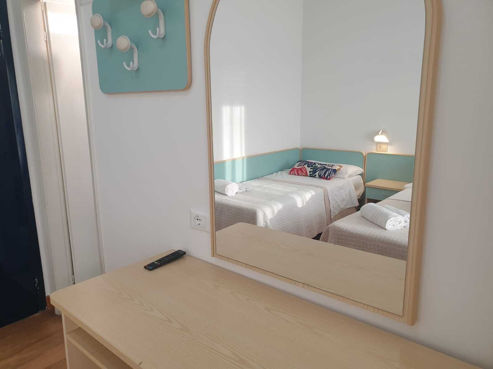 Quarto com duas camas, uma escrivaninha de madeira, um espelho e uma luminária na parede.