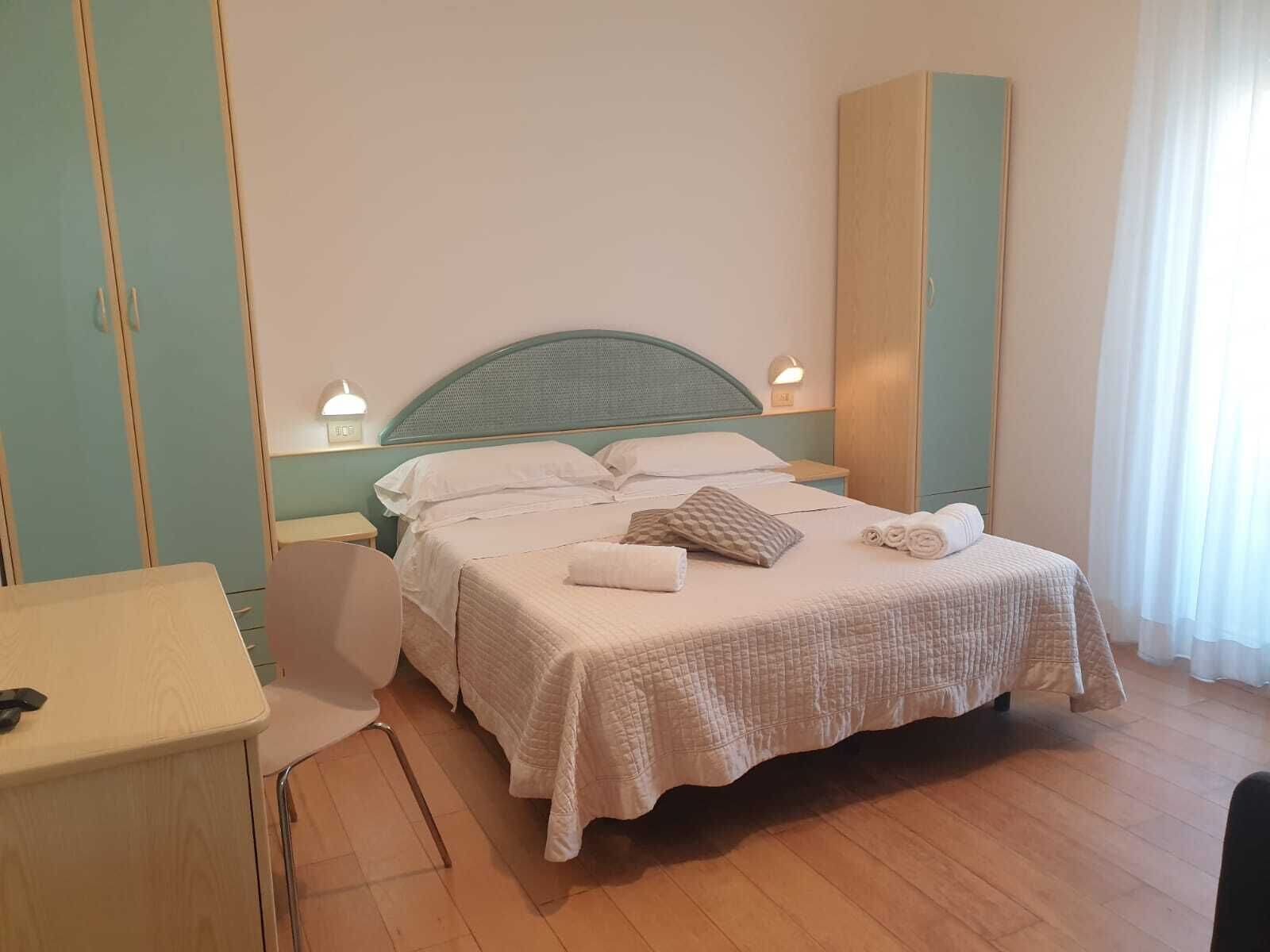 A neatly made bed with a quilted cover, a bedside table with a lamp, and a tall cabinet against the wall.