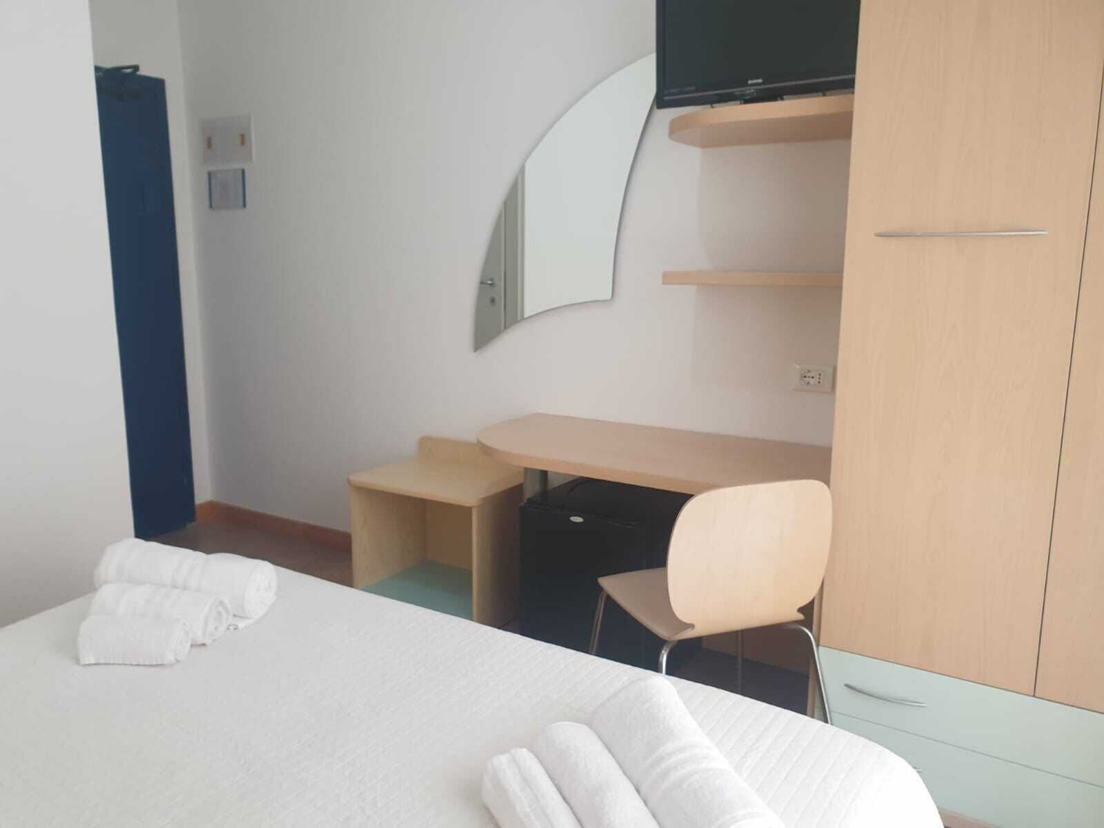 A hotel room with a bed, a desk, a chair, a TV, and a wardrobe.