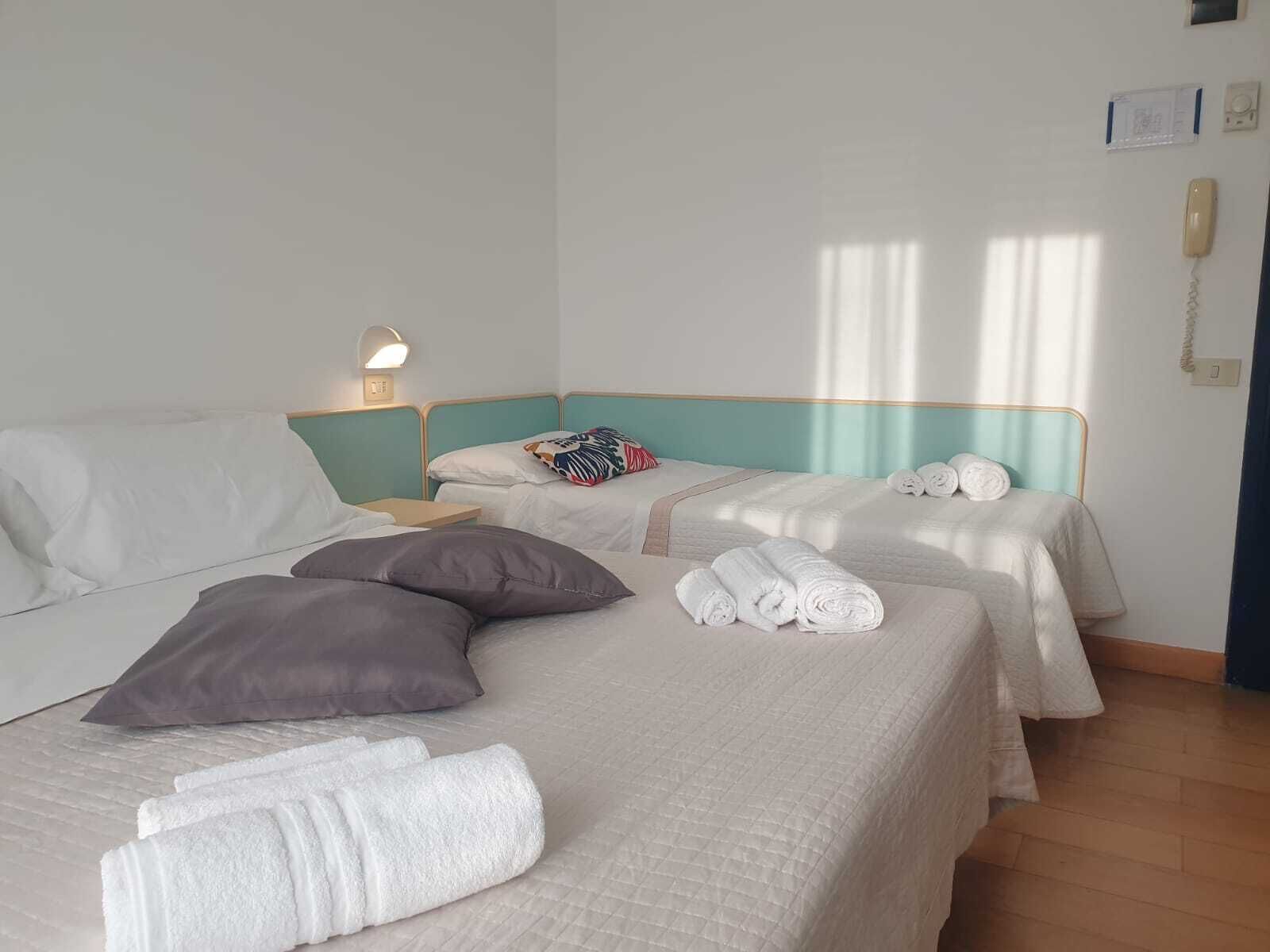 A hotel room with two beds, each with a pillow, a bedside lamp, and rolled towels.