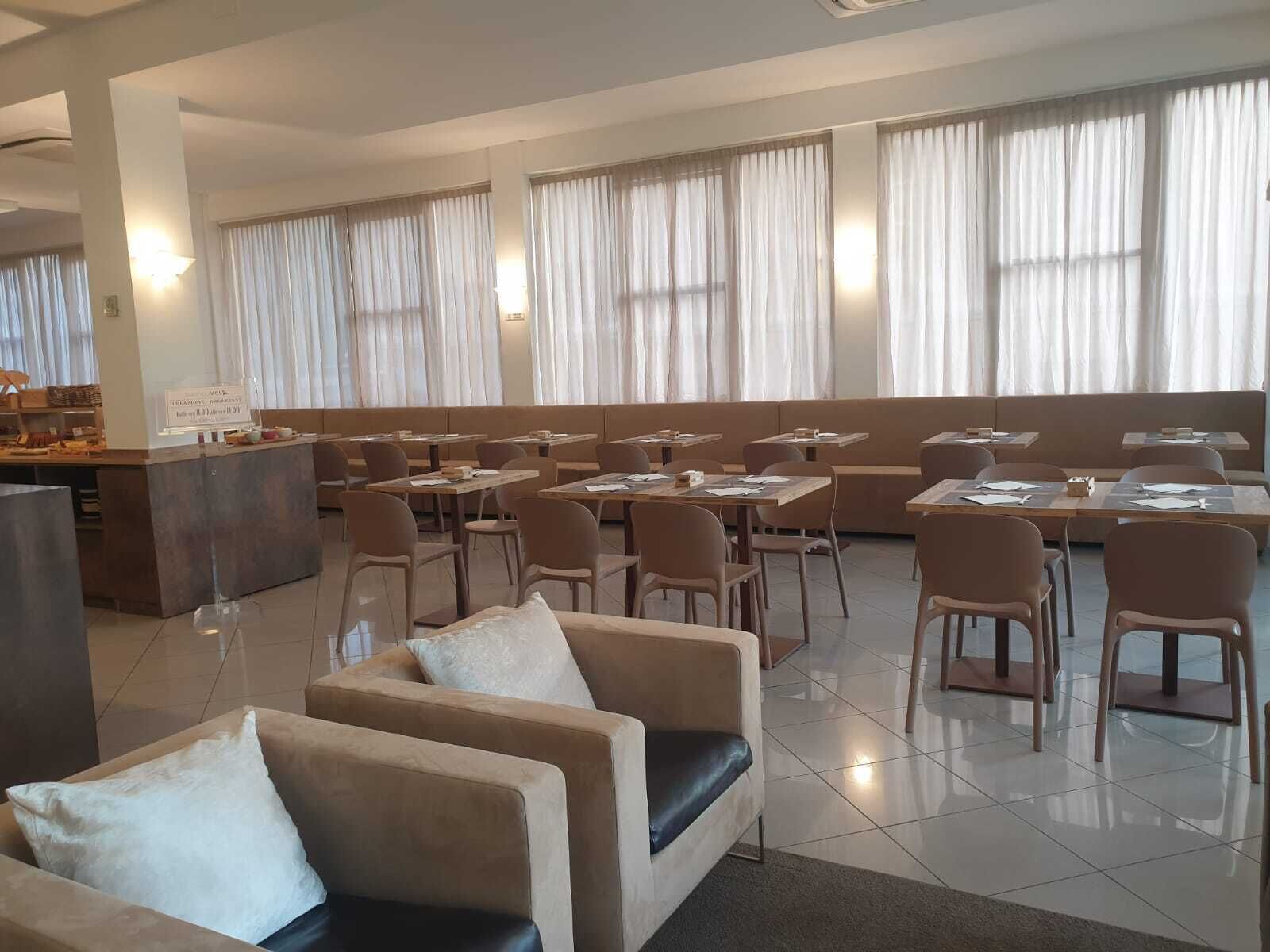 Un'ampia sala da pranzo con diversi tavoli e sedie, un bancone con il menu e ampie finestre con tende.