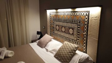 Una habitación de hotel con una cama grande, cabecera con diseño geométrico, lámpara de noche y una toalla en el suelo.
