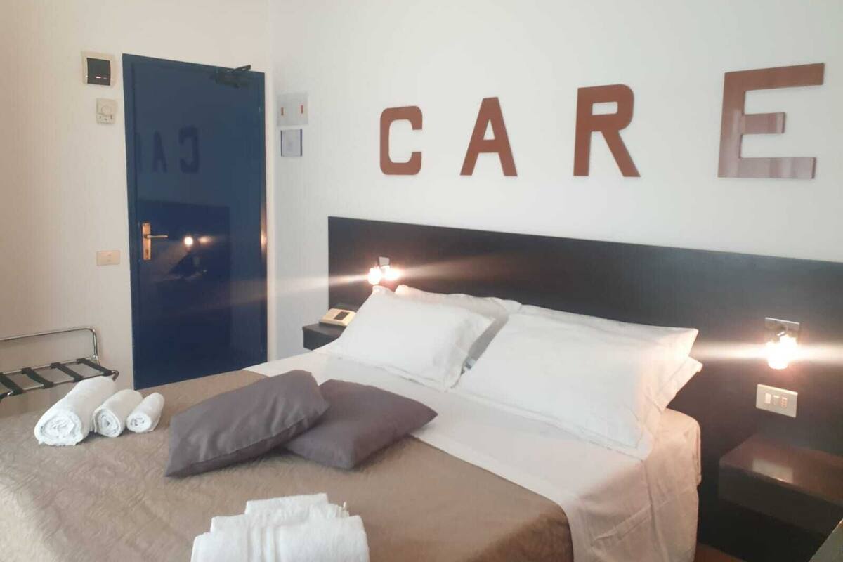 Ein Hotelzimmer mit einem Bett, Kissen, einem Nachttisch, einem Telefon und einer Wand mit dem Wort "CARE" in großen Buchstaben.