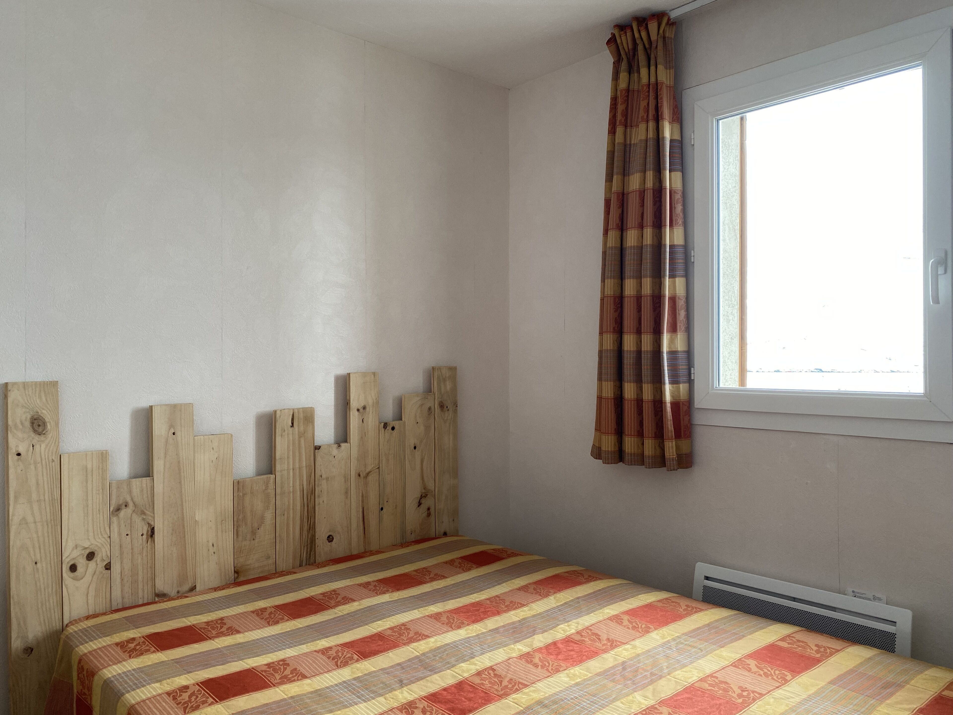 Ein Schlafzimmer mit einem hölzernen Kopfteil, einem Fenster mit Vorhang und einer Heizung.