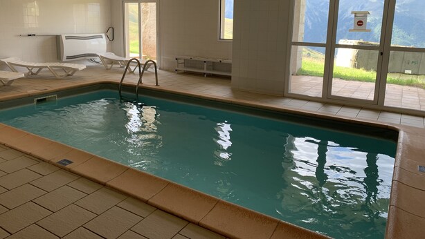 Une piscine intérieure avec des parois en verre transparent, des chaises longues et une vue sur l’extérieur.
