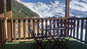 Une terrasse en bois avec une table et des chaises, d’où l’on a une vue sur une montagne enneigée.