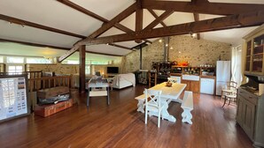 A spacious kitchen with wooden beams, a dining area with white furniture, and a stone wall backsplash. - Charming 4* gite swimming pool and spa  (Le Fossat)